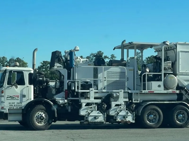 Workers operating pavement striping machinery on asphalt, applying white lines under cloudy sky