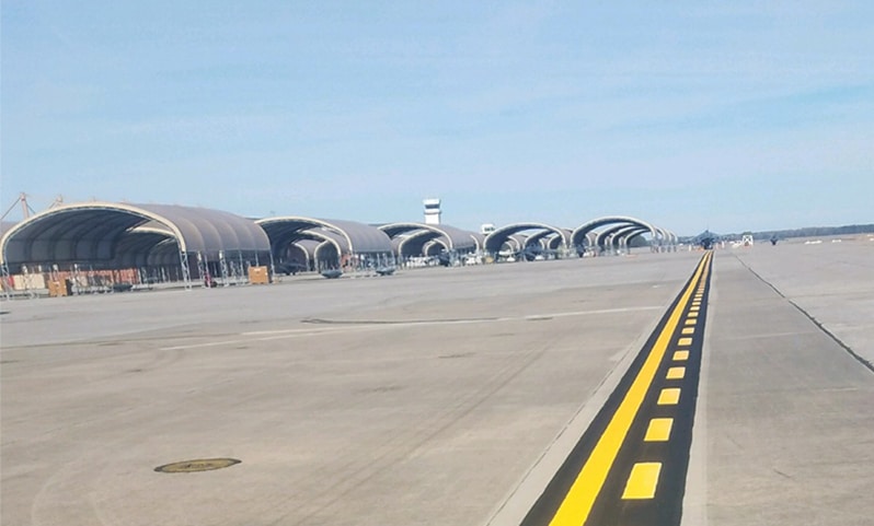 Airfield apron and taxiway pavement with yellow and white runway markings on concrete surface under clear sky