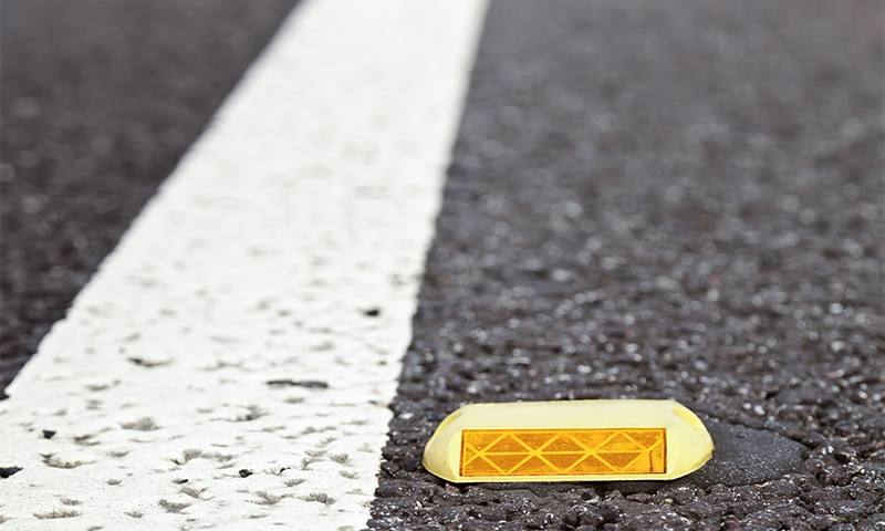 Close-up of reflective pavement markers (raised road studs) embedded in asphalt, capturing light against a dark surface